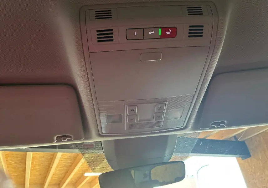 Vue intérieure du plafond avant du Skoda Kodiaq gris, montrant les commandes d'éclairage et le bouton SOS au centre.