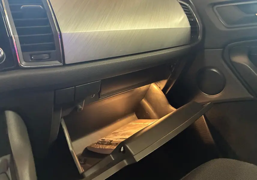 Intérieur du Skoda Kodiaq 2023, vue sur la boîte à gants ouverte avec éclairage intérieur et tableau de bord gris.