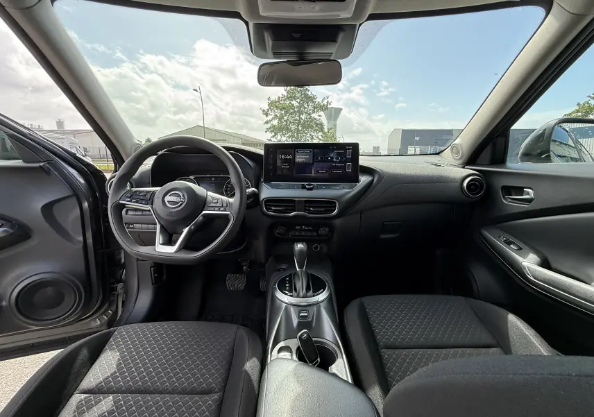 Vue intérieure avant du Nissan Juke Hybrid 2025 gris, montrant le volant, tableau de bord et écran tactile central.