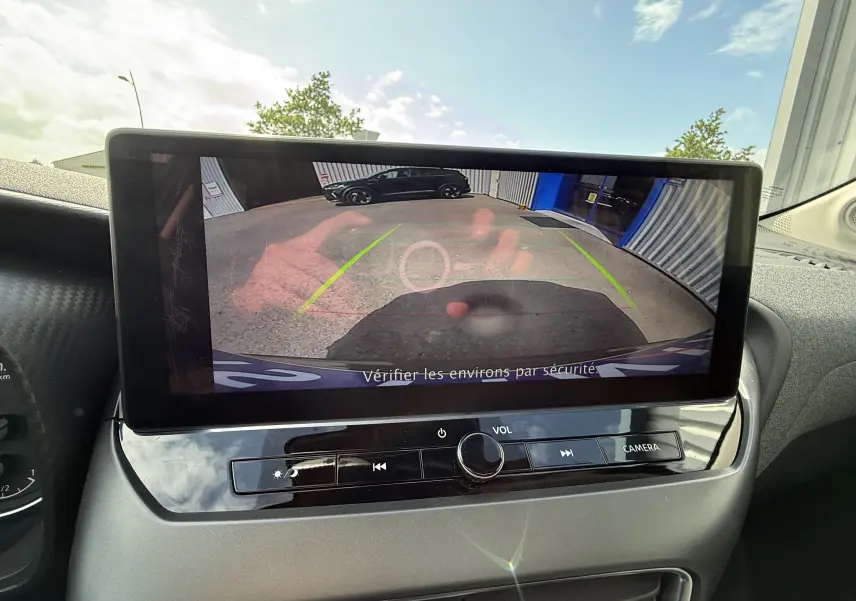 Écran central du Nissan Juke Hybrid 2025 montrant la caméra de recul avec vue arrière sur un véhicule noir et un bâtiment.