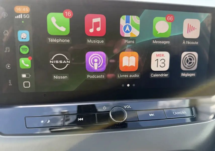 Écran tactile central du Nissan Juke Hybrid 2025 affichant les applications Apple CarPlay avec commandes volume et caméra en dessous.