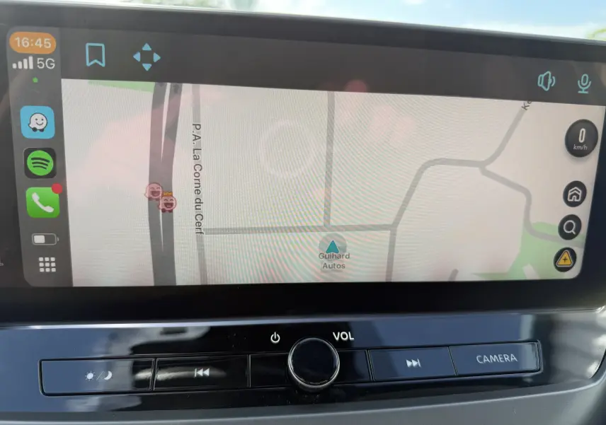 Écran tactile central du Nissan Juke Hybrid 2025 montrant la navigation avec commandes volume et caméra en dessous.