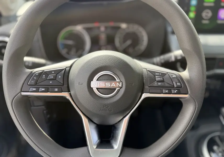 Gros plan sur le volant noir du Nissan Juke Hybrid 2025, avec commandes intégrées et logo central visible.