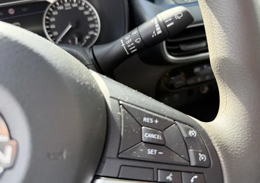 Gros plan sur le volant gris clair du Nissan Juke Hybrid 2025, avec commandes de régulateur de vitesse et commodo d’essuie-glace visible.