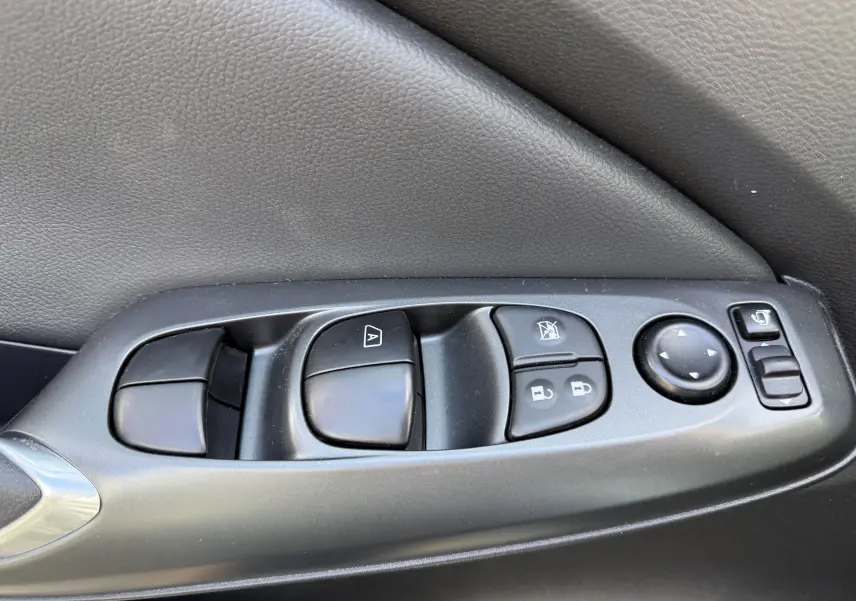 Gros plan sur les commandes de lève-vitres et rétroviseurs côté gauche intérieur d’un Nissan Juke gris squale métal 2025.