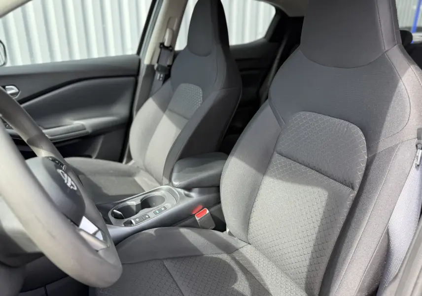 Vue intérieure côté conducteur du Nissan Juke Hybrid 2025, sièges tissu gris clair avec motifs géométriques.
