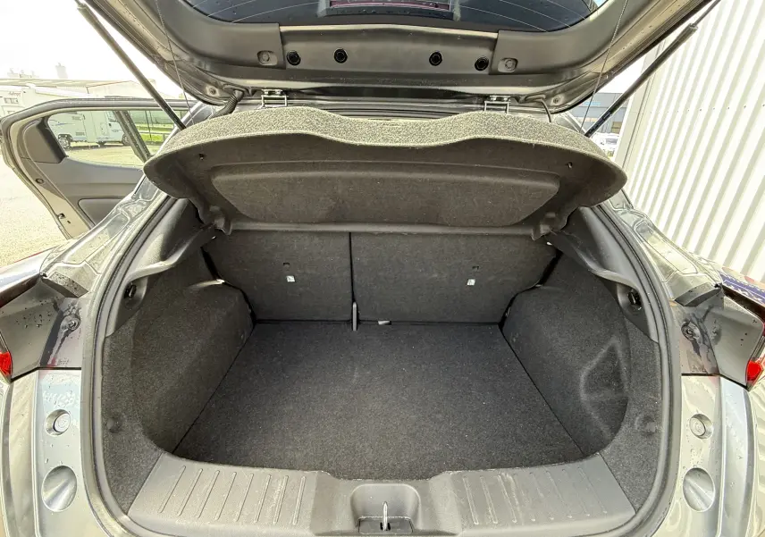 Coffre ouvert vu de l'arrière d'un Nissan Juke gris squale métal, montrant l'espace de chargement vide et la trappe de coffre relevée.