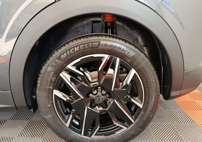 Gros plan sur la roue avant gauche du Peugeot 3008 gris foncé, mettant en valeur la jante noire brillante et le pneu Michelin e-Primacy.