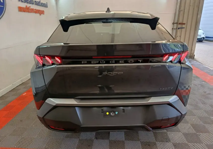 Vue arrière d'un Peugeot 3008 gris foncé hybride 2025 avec feux LED distinctifs et hayon fermé dans un garage.