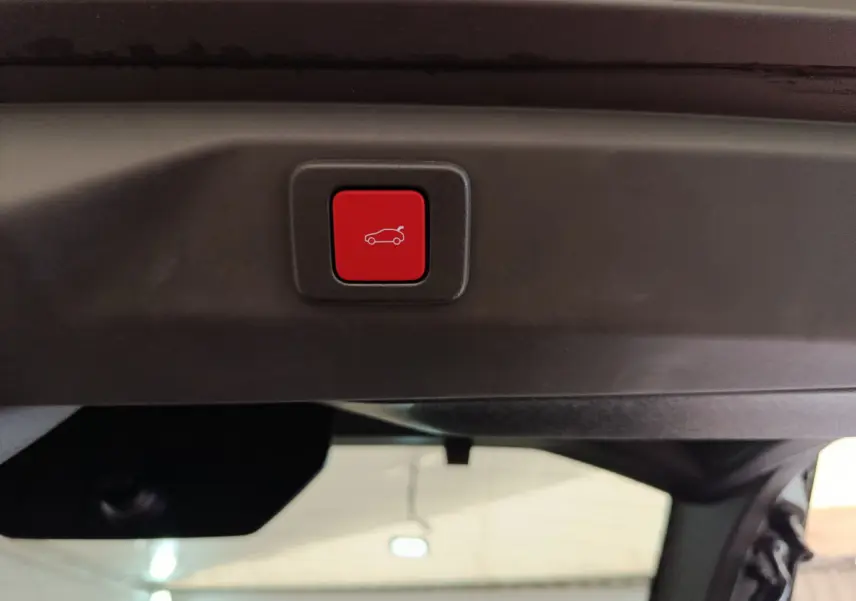 Bouton rouge d'ouverture électrique du coffre sur le hayon intérieur d'un Peugeot 3008 gris foncé hybride 2025