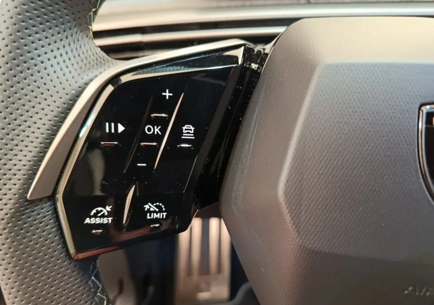 Gros plan sur les commandes noires du volant cuir perforé côté gauche du Peugeot 3008 gris foncé 2025.