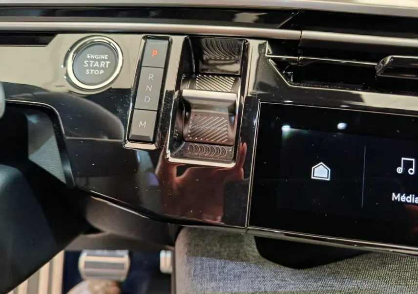 Détail de la console centrale noire brillante du Peugeot 3008 hybride 2025 avec bouton start/stop et commandes de boîte automatique.