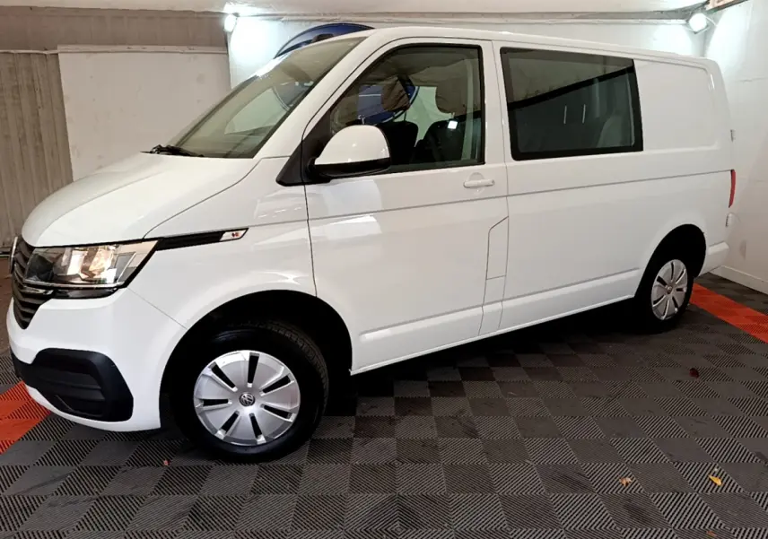 Vue 3/4 avant droit d’un Volkswagen Transporter blanc 2021 avec jantes acier et vitres teintées arrière.
