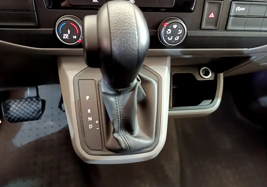 Gros plan sur le levier de vitesses automatique noir et gris du Volkswagen Transporter 2.0 TDi 150 DSG7, tableau de bord beige.