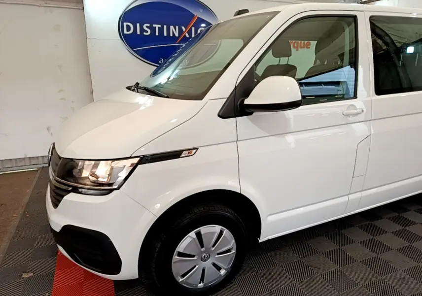 Vue 3/4 avant droit d'un Volkswagen Transporter blanc avec phares allumés et jantes acier avec enjoliveurs.