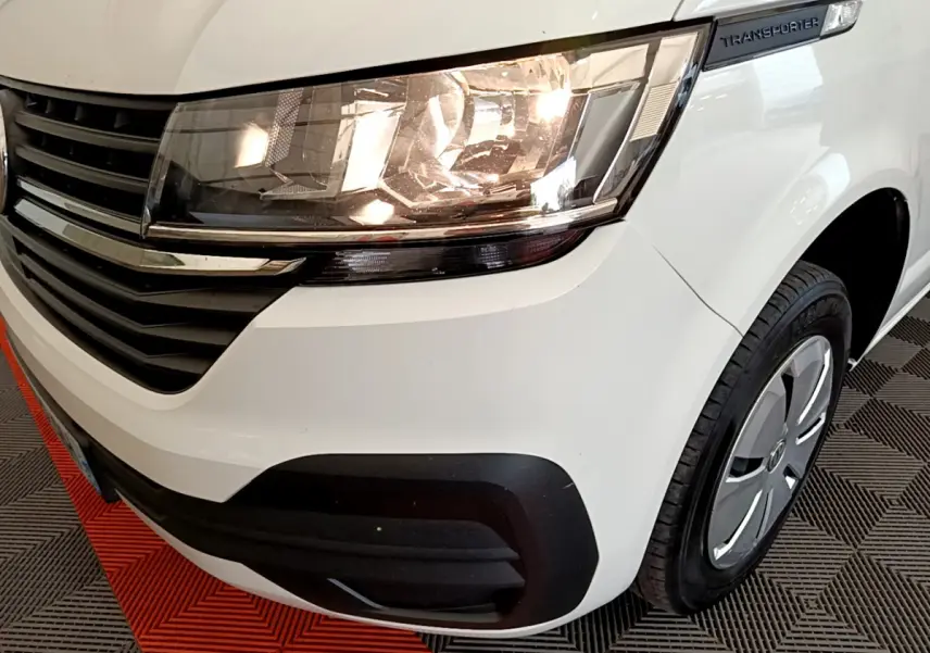 Gros plan sur l'avant droit du Volkswagen Transporter blanc, mettant en valeur le phare allumé et la calandre noire.