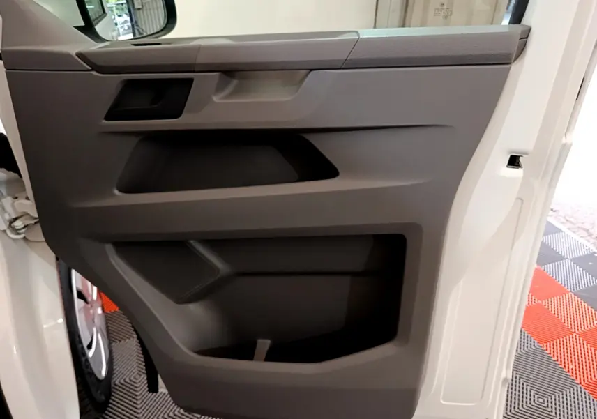 Vue rapprochée de la porte intérieure côté conducteur du Volkswagen Transporter blanc, avec panneau gris et rangement intégré.