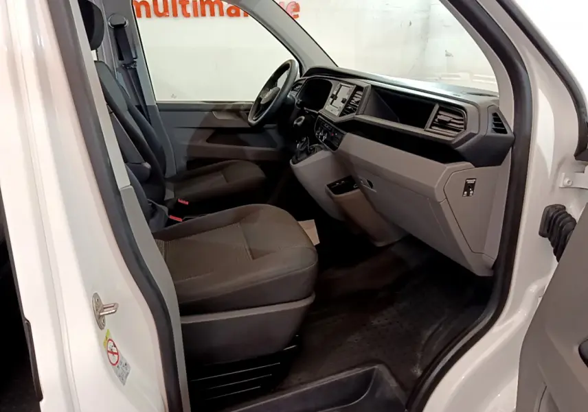 Vue intérieure côté conducteur du Volkswagen Transporter blanc 2021, montrant sièges et tableau de bord moderne.