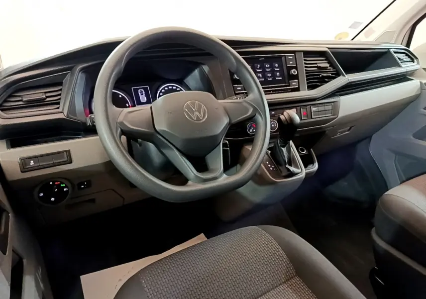 Vue intérieure avant du tableau de bord et volant noir du Volkswagen Transporter blanc, avec écran tactile central et levier de vitesses.