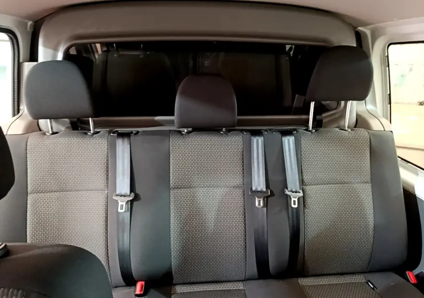 Vue intérieure arrière montrant la banquette trois places grise du Volkswagen Transporter blanc avec ceintures de sécurité.