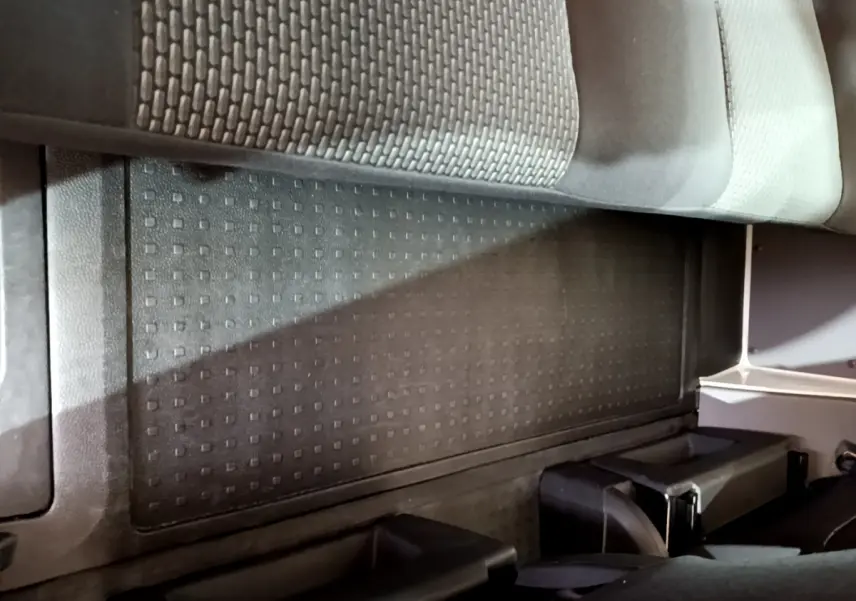 Vue intérieure du plancher arrière avec tapis caoutchouc noir et partie inférieure des sièges du Volkswagen Transporter blanc.