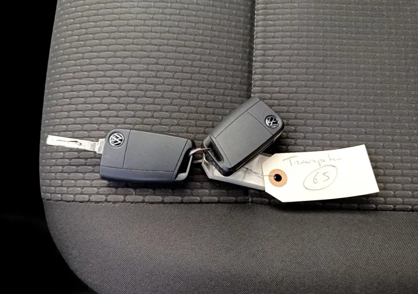 Clé Volkswagen posée sur un siège tissu gris foncé à motifs, avec une étiquette manuscrite attachée.