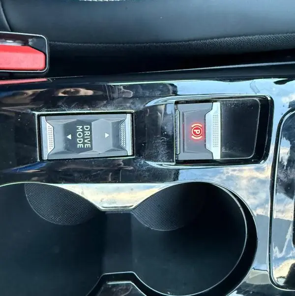 Gros plan sur la console centrale noire du Peugeot 208 Hybrid 110, montrant le bouton Drive Mode et le frein à main électrique allumé.
