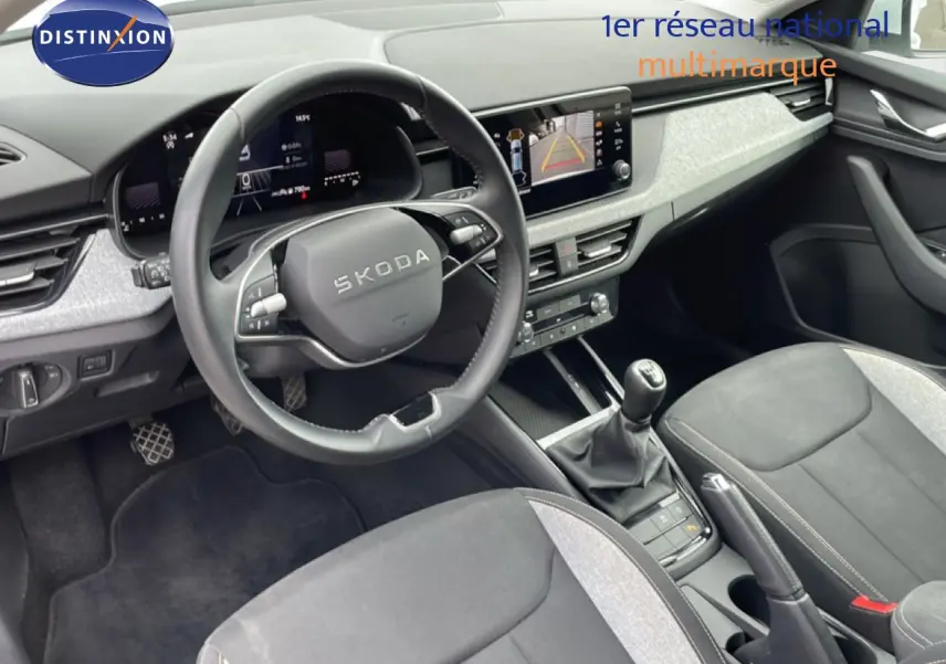 Vue intérieure côté conducteur de la Skoda Scala blanc glacier 2025, volant cuir, tableau de bord digital et levier de vitesse manuel.
