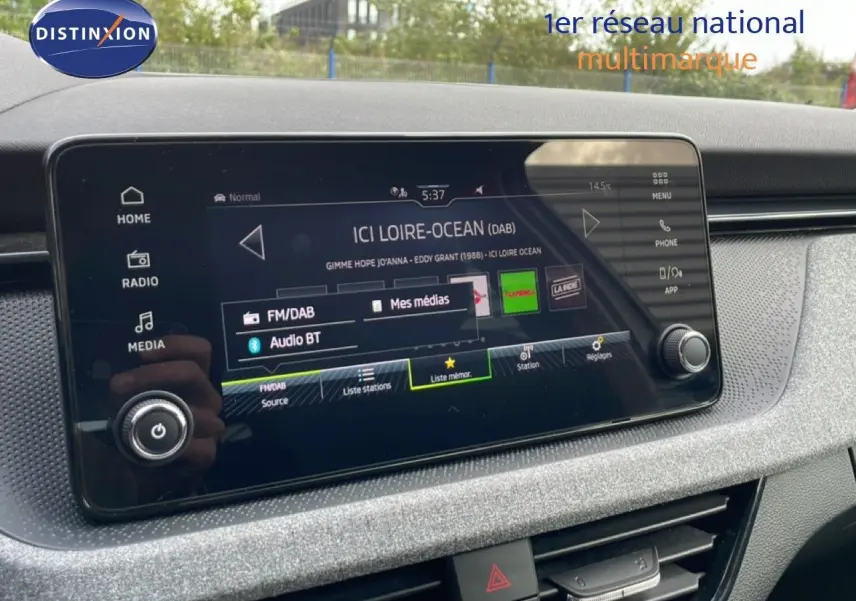 Écran tactile central du Skoda Scala blanc glacier 2025, affichant la radio FM/DAB avec interface moderne et boutons tactiles.