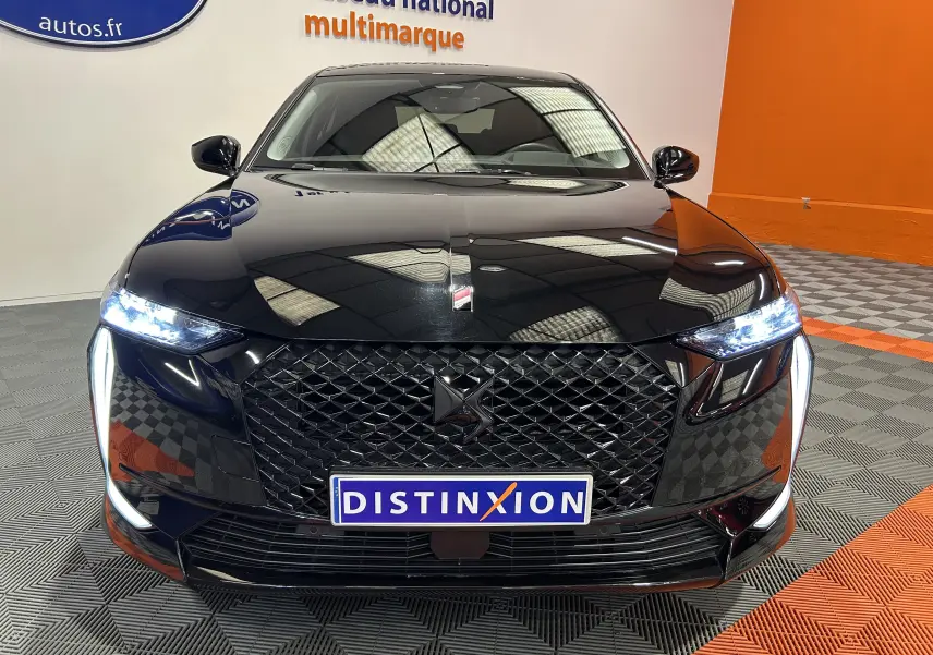 Vue de face d'une DS4 noire Perla Nera avec calandre distinctive et feux LED allumés dans un showroom.
