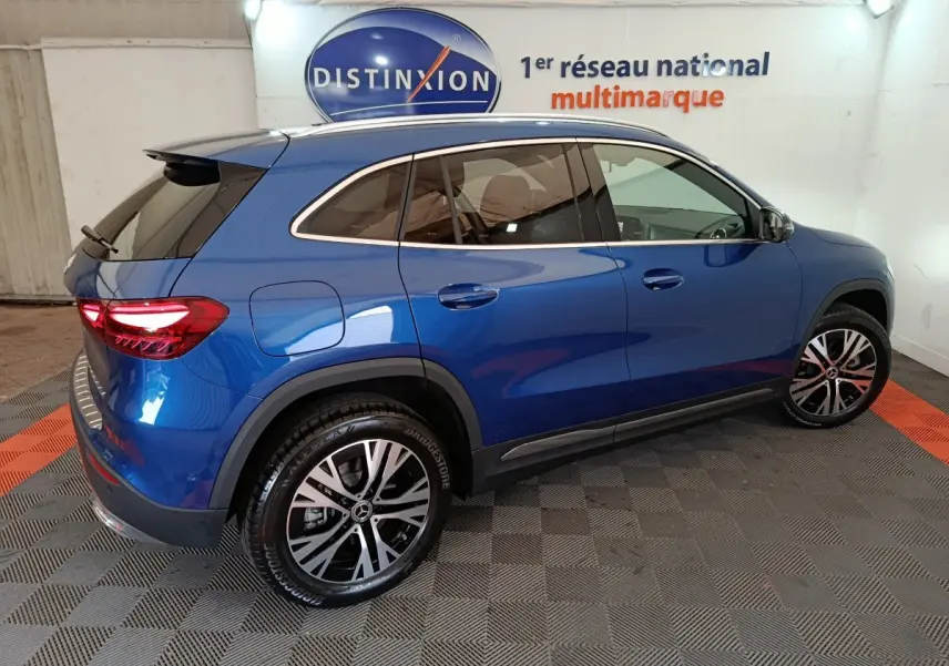 Vue 3/4 arrière droite d'un Mercedes GLA 250 e Business Line bleu avec jantes alliage et toit noir dans un showroom.