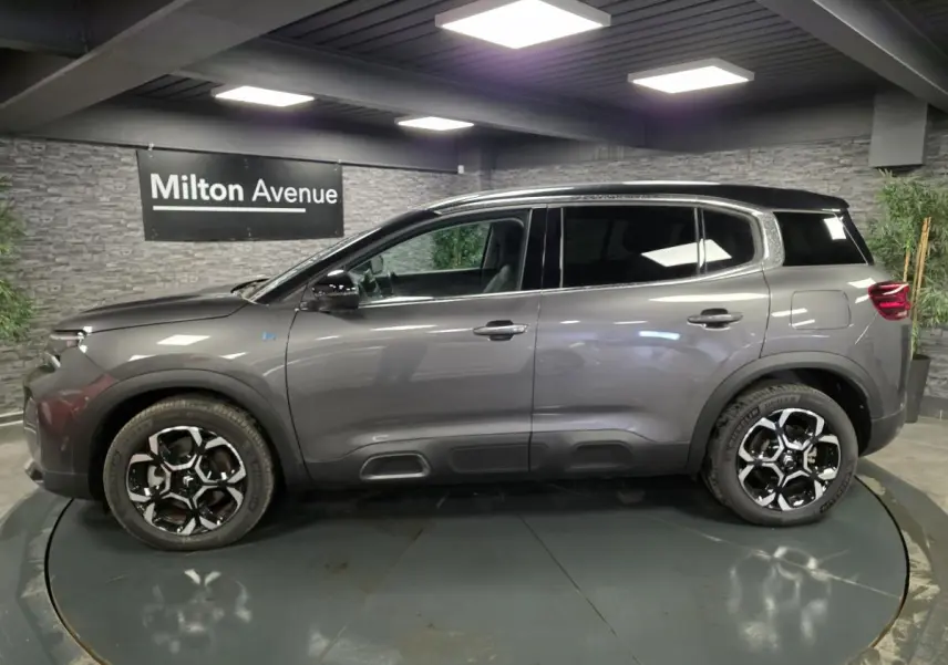 Profil côté gauche du Citroën C5 Aircross Hybrid gris avec toit noir et jantes alliage bi-ton dans un showroom.