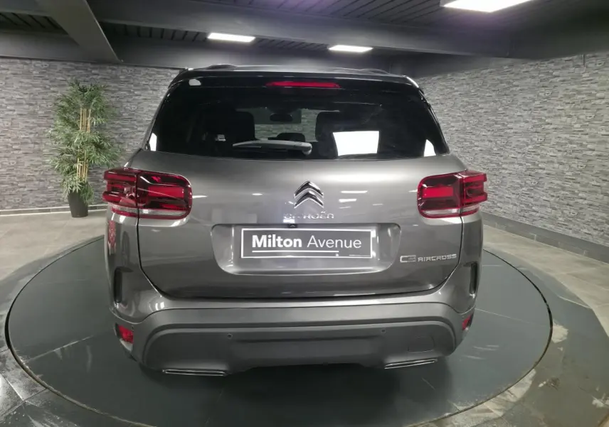Vue arrière d'un Citroën C5 Aircross gris métallisé avec toit noir et feux arrière LED en intérieur showroom.