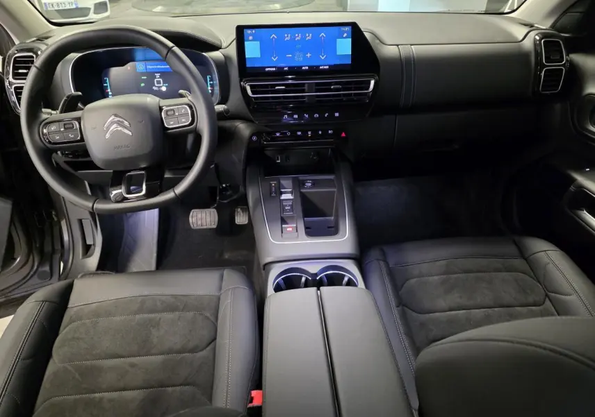 Intérieur noir du Citroën C5 Aircross Hybrid 2024, vue avant sur volant, tableau de bord et console centrale tactile.