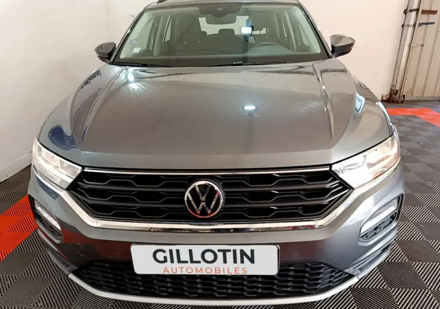 Vue avant d’un Volkswagen T-Roc gris foncé avec calandre noire et phares allumés dans un garage.