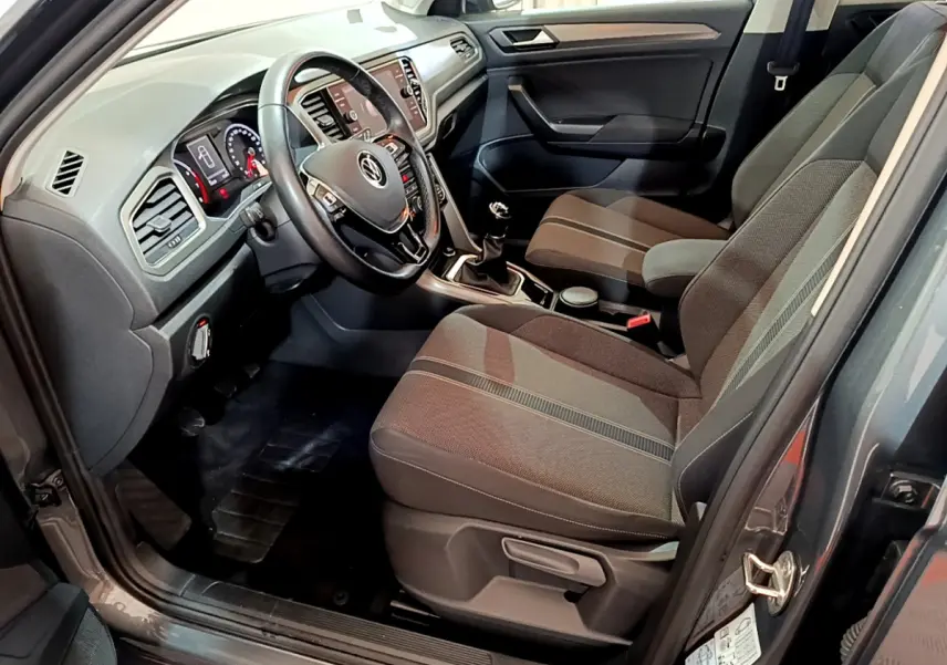 Vue intérieure côté conducteur du Volkswagen T-Roc gris foncé 2021, montrant le volant cuir, tableau de bord digital et sièges tissu.