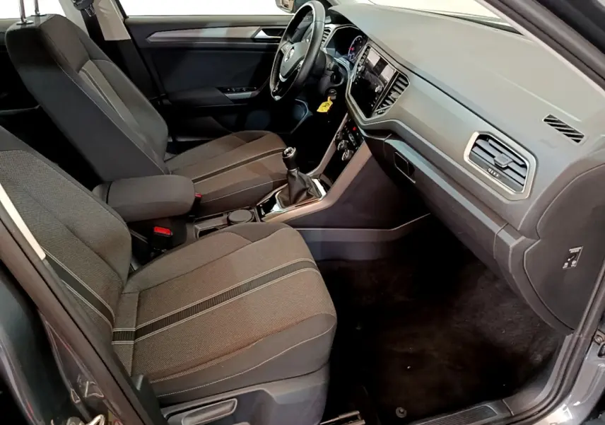 Vue intérieure côté passager avant du Volkswagen T-Roc gris foncé, montrant les sièges tissu et la console centrale avec boîte manuelle.
