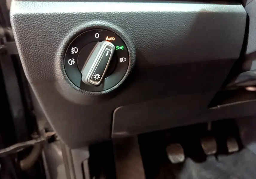 Gros plan sur la commande des phares du Volkswagen T-Roc 1.0 TSI 110 Lounge, intérieur noir.