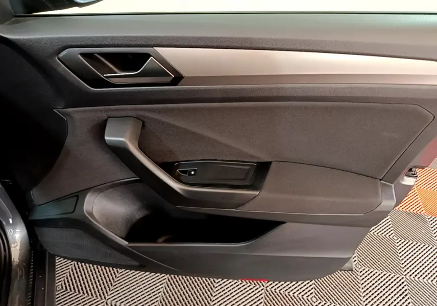 Vue intérieure côté gauche de la porte avant gris foncé du Volkswagen T-Roc 1.0 TSI 110 Lounge avec poignée et panneau noir.