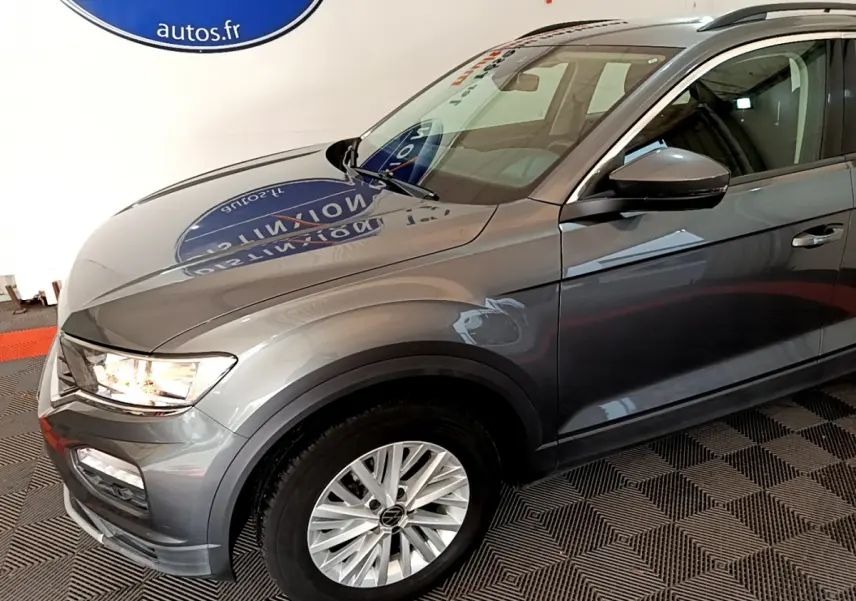 Vue 3/4 avant droit d’un Volkswagen T-Roc gris foncé avec jantes alliage et feux allumés dans un showroom.