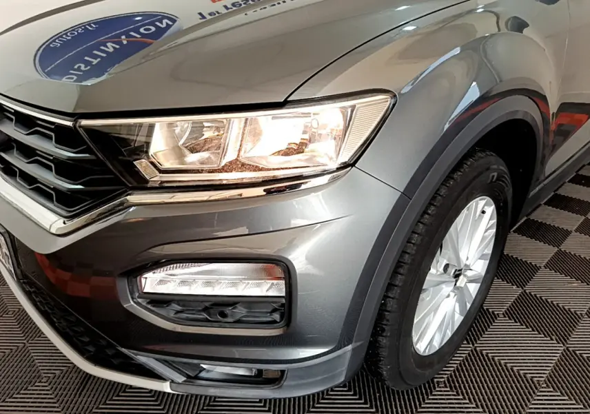Gros plan sur l'avant droit du Volkswagen T-Roc gris foncé, mettant en valeur le phare allumé et la roue avant.