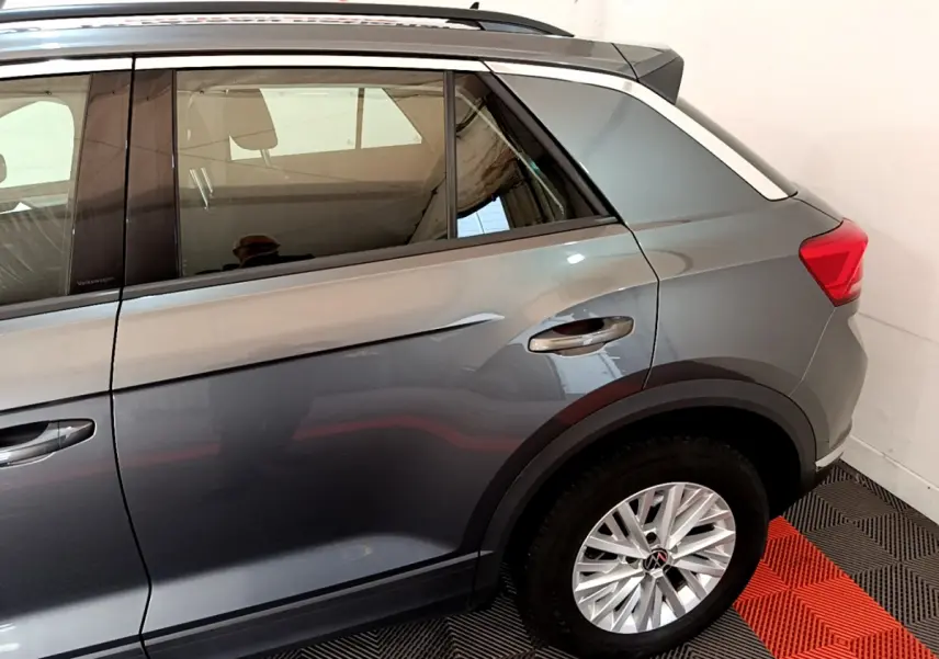 Vue latérale arrière droite d’un Volkswagen T-Roc gris foncé avec jante alliage et barres de toit noires.