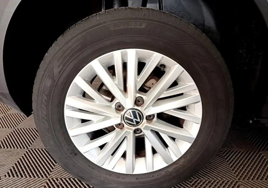 Gros plan sur la roue avant droite avec jante argentée et logo Volkswagen sur un Volkswagen T-Roc gris foncé.