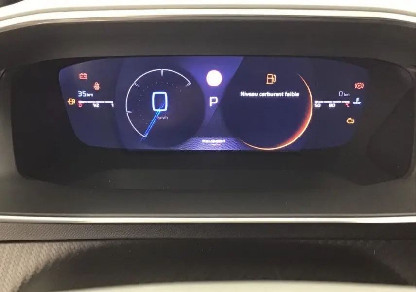 Tableau de bord numérique de la Peugeot 2008 Hybrid 145ch GT, affichant vitesse à 0 km/h et alerte niveau carburant faible.