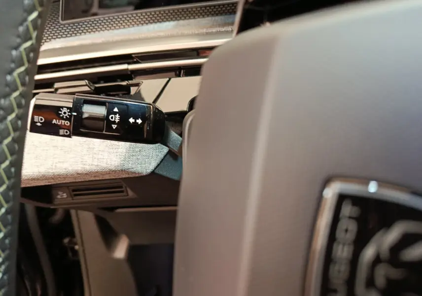 Gros plan sur la manette de commandes d'éclairage à gauche du volant gris clair du Peugeot 3008 noir.