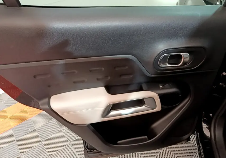 Vue rapprochée de la porte intérieure côté gauche du Citroën C5 Aircross Hybrid 225 noir, avec accoudoir beige et poignée chromée.
