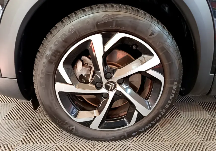 Gros plan sur la roue avant gauche noire du Citroën C5 Aircross Hybrid avec jante alliage bicolore et logo Citroën central.