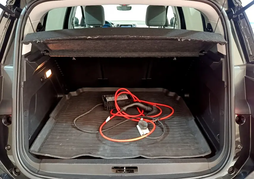 Coffre ouvert vu de l'arrière d'une Citroën C5 Aircross Hybrid noire avec câble de recharge rouge visible.