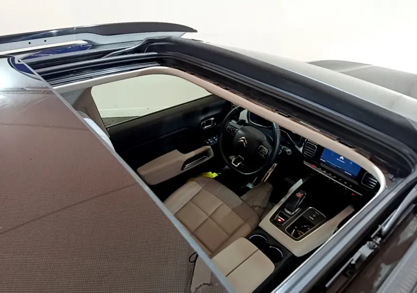 Vue intérieure par le toit ouvrant d'un Citroën C5 Aircross Hybrid noir, montrant le tableau de bord et sièges beige.