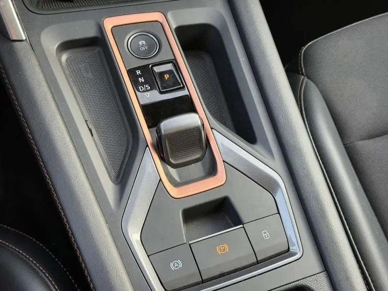 Vue rapprochée de la console centrale du SEAT LEON 2025 avec levier de boîte auto entouré d’un cadre cuivré.